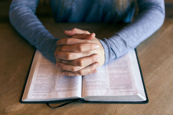 main jointe au dessus d'une bible ouverte
